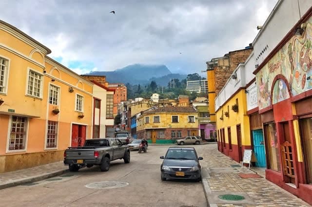 A shot of a street in La Candelaria, with older and more traditional buildings, painted in yellow and other bright colours. High hills can be seen in the background