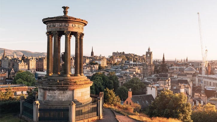 A view looking down at Edinburgh City from Calton Hill during sunset. Edinburgh castle is visible. 